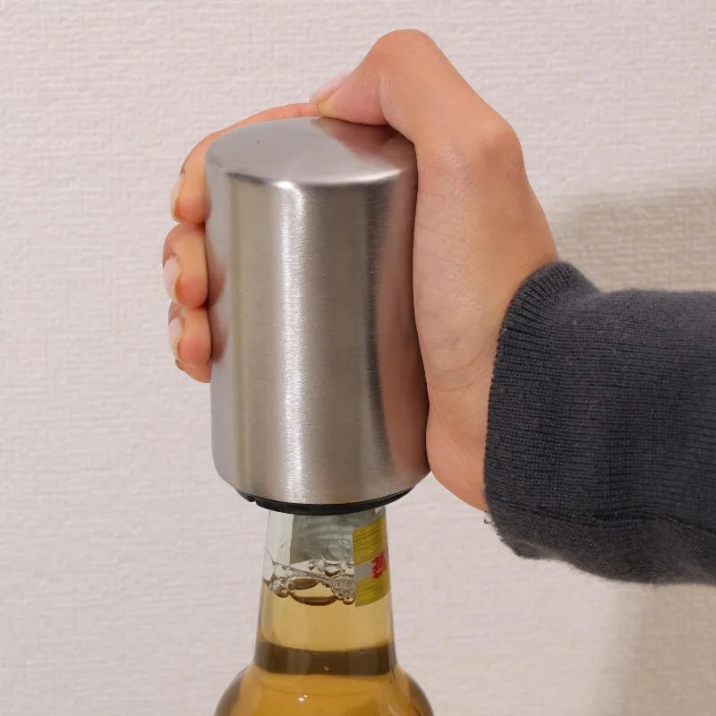 Une main tient un ouvre-bouteille magnétique en acier inoxydable attaché à une bouteille en verre.