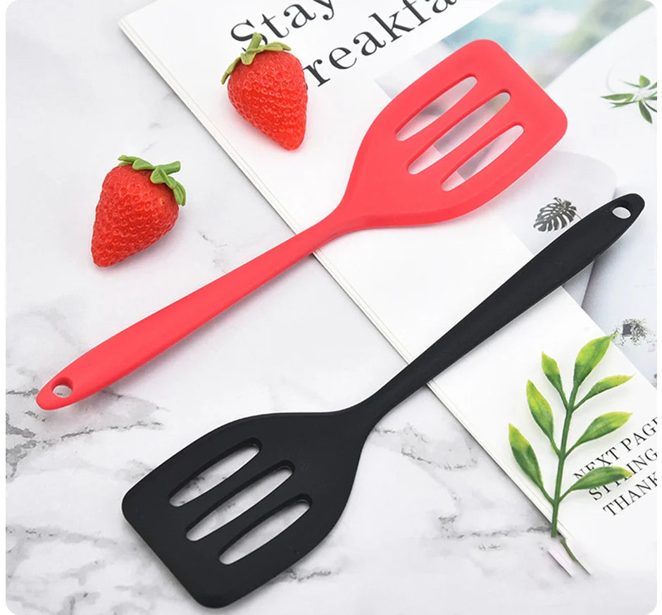 A red silicone flat bottom frying spatula and a black silicone spatula are displayed on a white marble surface.