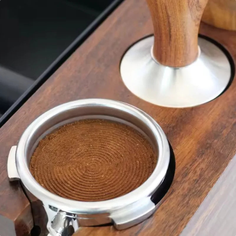A precision espresso tamper set featuring a stainless steel cup and a wooden handle resting on a dark wood surface.