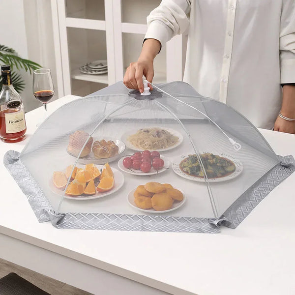 A clear mesh food cover is placed on a white table, containing various food items like fruit and pastries.