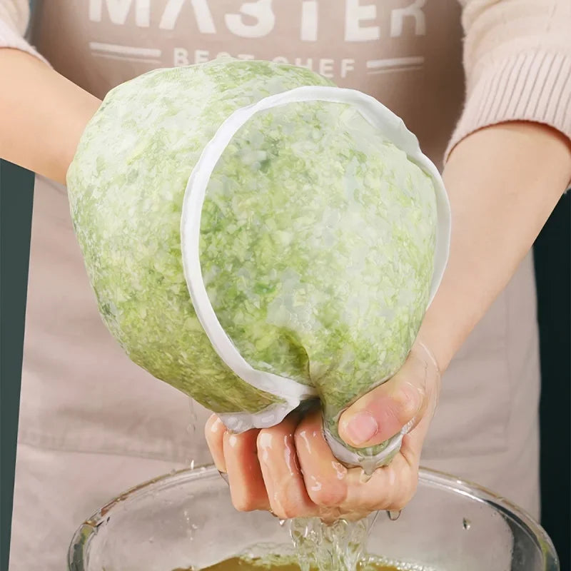 A hand holds a reusable fine mesh pour filter bag filled with green liquid over a glass bowl.