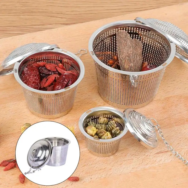 A silver stainless steel tea leaf infuser filter is shown with dried tea leaves in a metal container on a wooden surface.