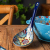 A blue and white ceramic serving spoon with a decorative handle rests on a wooden table next to a matching bowl.