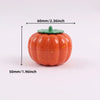 An orange pumpkin-shaped manual herb and spice grinder with a green lid.