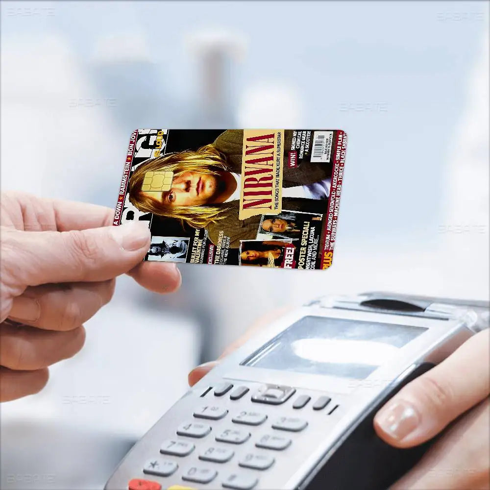 A hand holds a Nirvana band anime debit card with stickers against a blurred background.