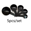 A set of five black precision kitchen measuring spoons with various capacities marked in grams.