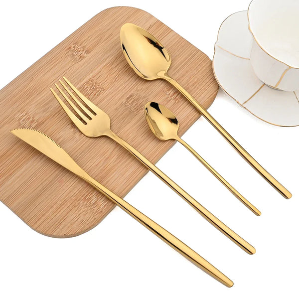 A set of gold-colored stainless steel cutlery including a spoon, fork, and knife placed on a wooden cutting board.