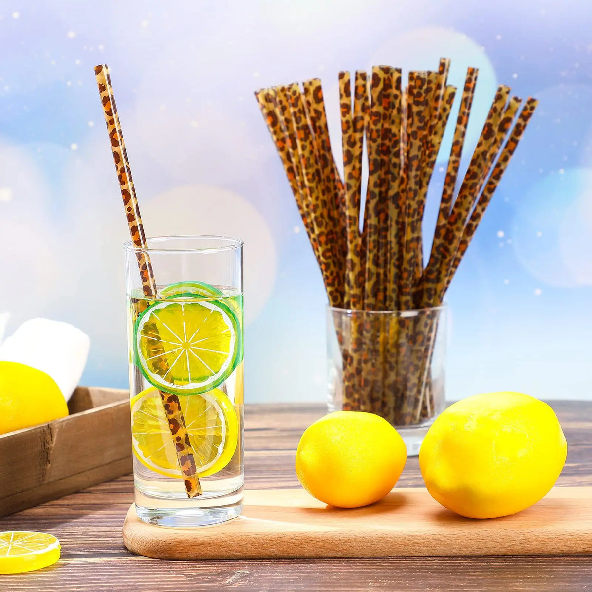 A glass of lemon water with a citrus slice and a striped straw next to a wooden cutting board.