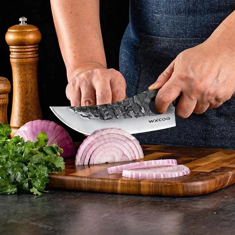 A hand is using a forged chef knife to slice red onions on a wooden cutting board.