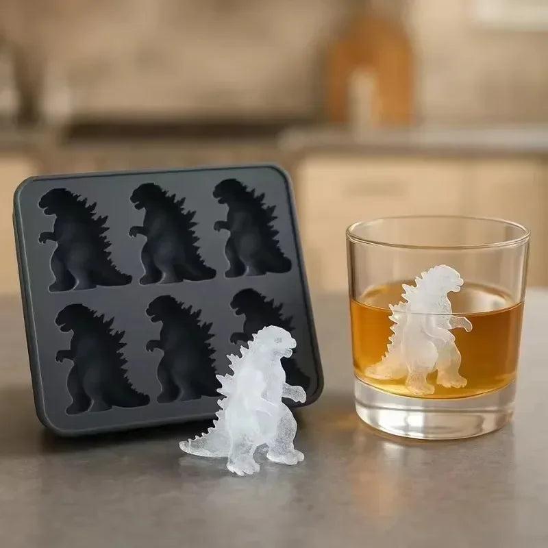 A set of dinosaur-shaped ice cubes in a dark gray tray next to a glass of amber liquid.