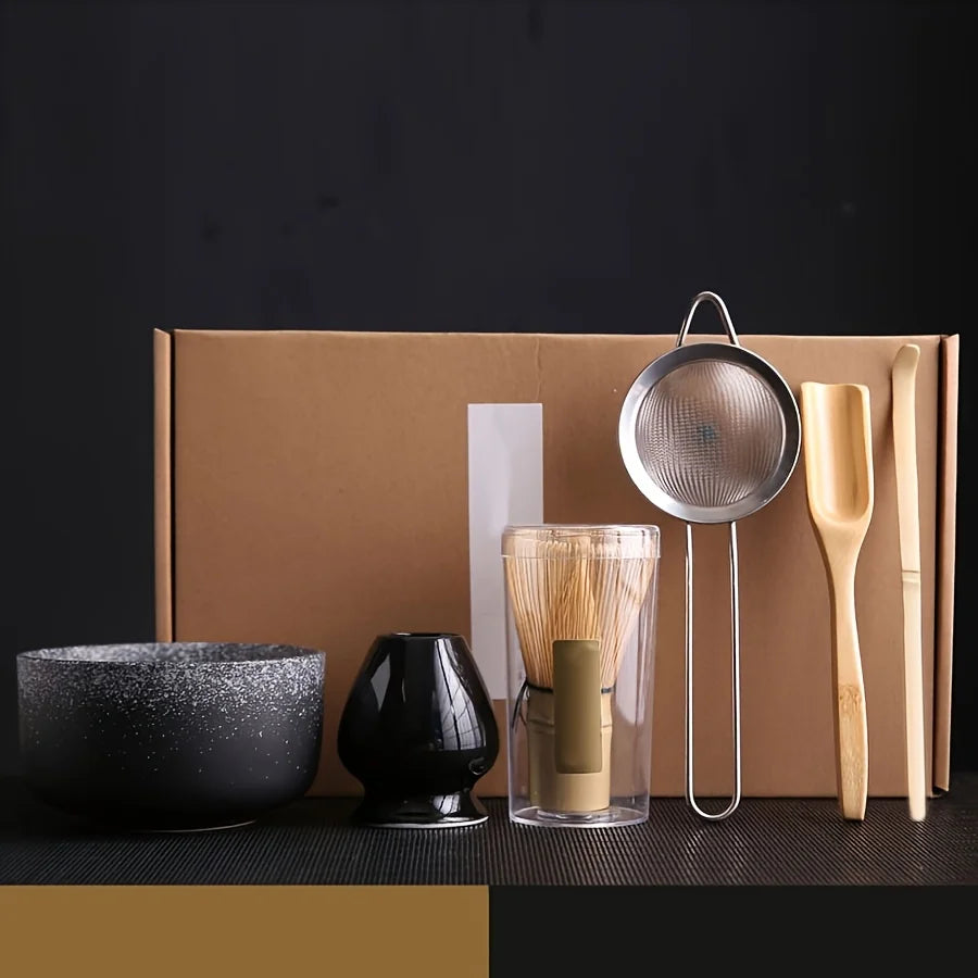A traditional Japanese matcha tea set featuring a black bowl, a black ceramic cup, a bamboo whisk, and a metal tea strainer d