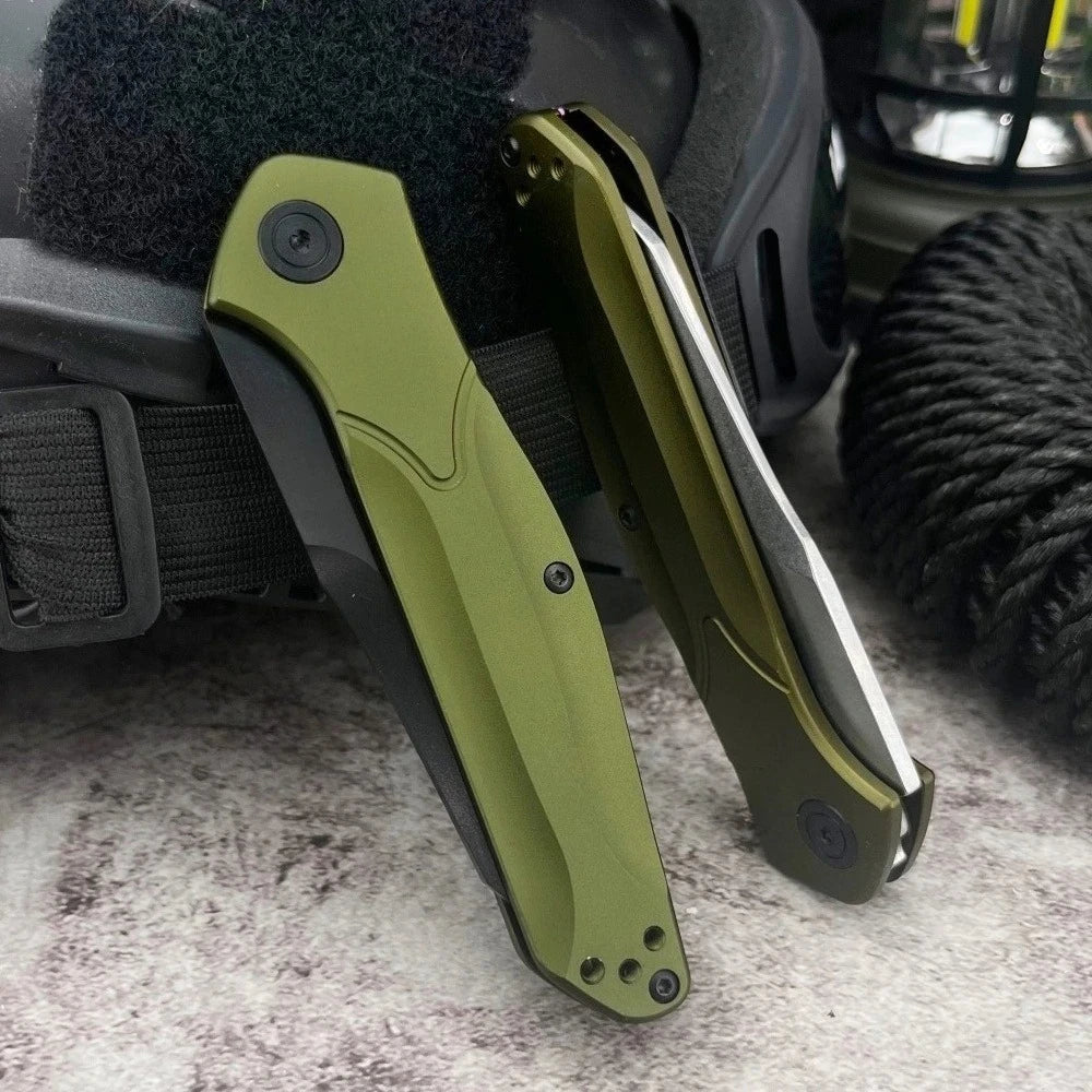 A folding pocket knife with a green blade is shown resting on a dark fabric and next to a black cord.