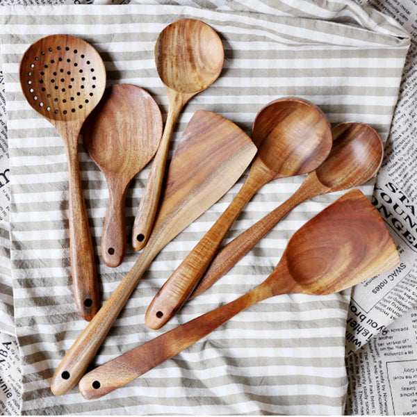 Set aus natürlichen Holz-Küchenutensilien, darunter Schöpflöffel, Spatel und Holzlöffel auf kariertem Tuch.