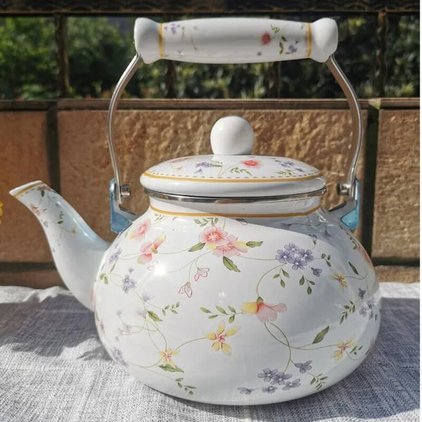 A white enamel teapot with a silver lid and a handle, decorated with floral patterns.
