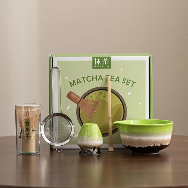 A green box containing a matcha tea set with a bamboo whisk, scoop, and bowl on a wooden surface.