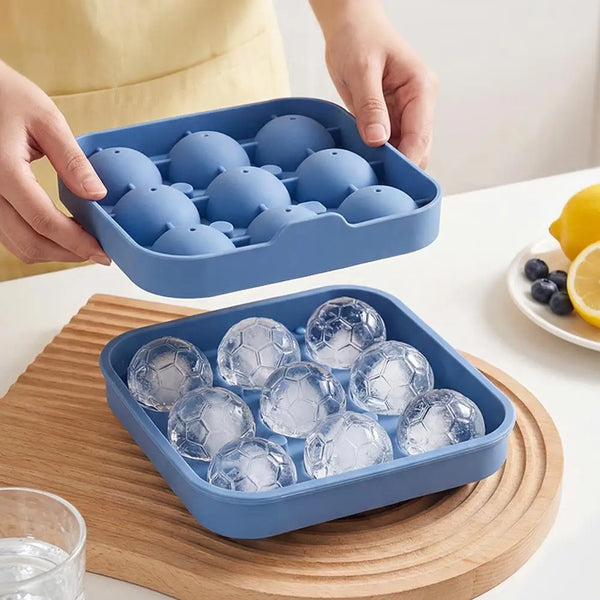 Eine Hand hält eine blaue Silikon-Eiswürfelform mit klaren Eiswürfeln auf einem Holzbrett.