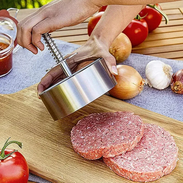 Eine Hand drückt Hackfleisch in eine Edelstahlpresse auf einem Holzschneidebrett.