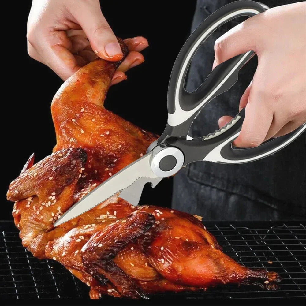 Hands are using heavy duty stainless steel kitchen scissors to cut a roasted chicken on a grill grate.