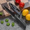 A black utility knife set with a stainless steel blade rests on a wooden cutting board surrounded by fresh tomatoes and lime 