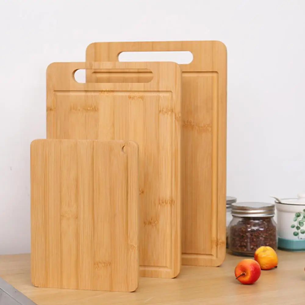 A set of three light wood bamboo kitchen cutting boards standing upright on a wooden surface.