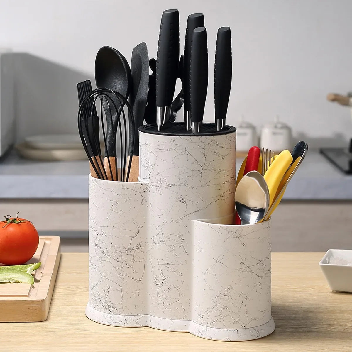 A cylindrical white marble kitchen utensil storage holder filled with various black and gold cooking tools.