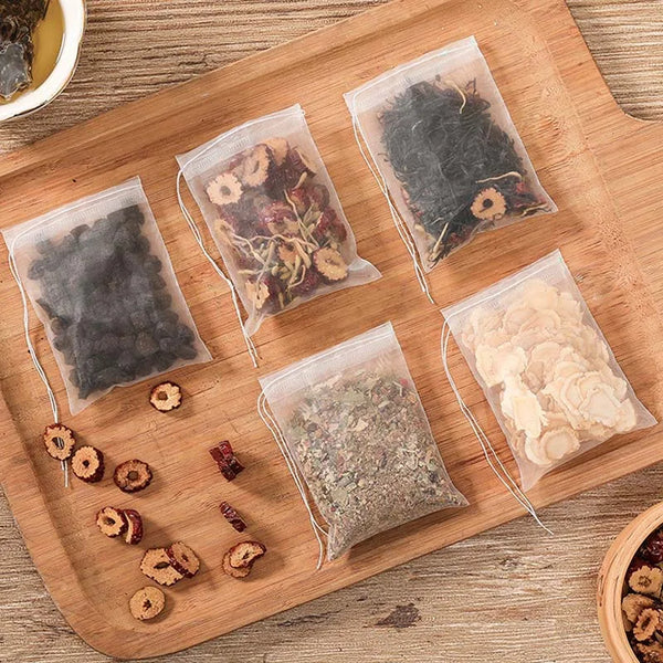 Several clear plastic bags filled with loose tea and spices are arranged on a wooden board.