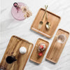 A natural acacia wood serving tray set featuring cutlery and a small bowl on a white marble surface.