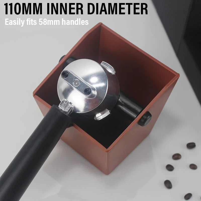 A silver espresso knock box with a black handle is shown inside a brown container.