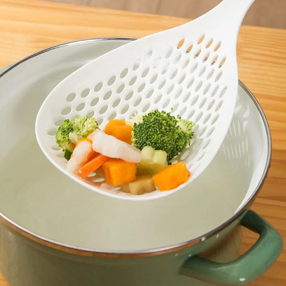 A white kitchen strainer and skimmer set is shown containing colorful vegetables like carrots, broccoli, and celery.