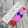 A set of silicone baking molds shaped like bows and flowers in various shades of pink, purple, and red.