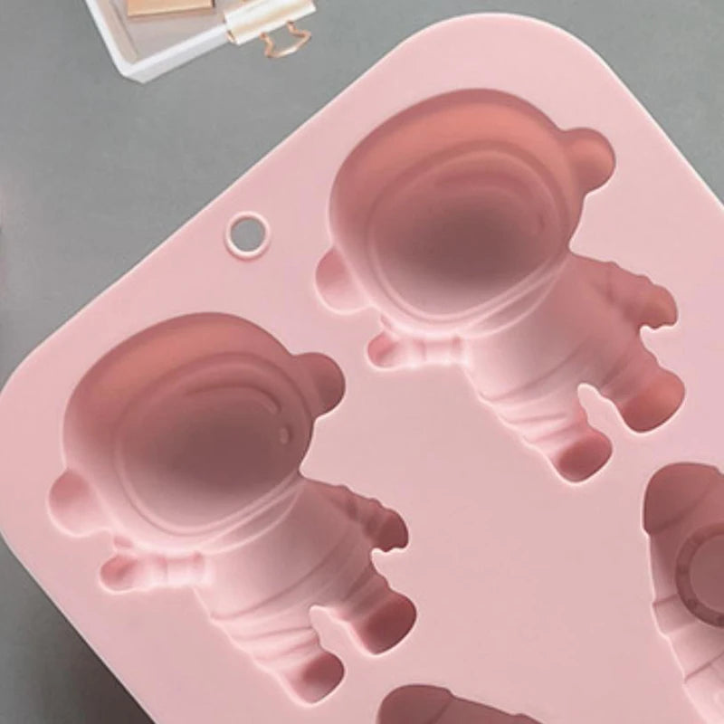 A pink silicone mold with multiple astronaut figures is shown on a gray surface.