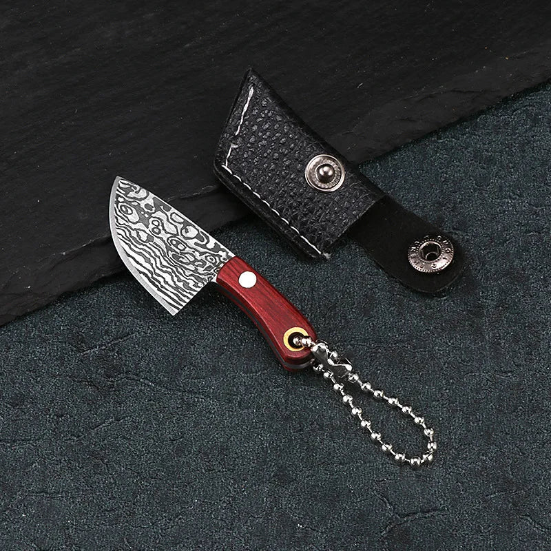 A set of Damascus pattern pocket mini knives with black leather sheaths and silver chain attached.