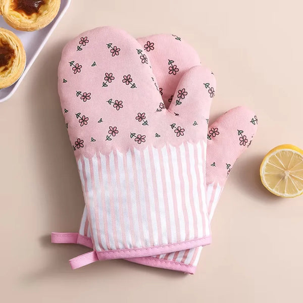 Pink knitted oven mitts with a floral pattern and striped cuffs are displayed on a light background.