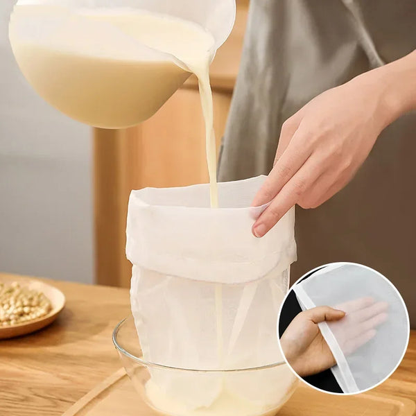 Eine Hand gießt Milch aus einem weißen Behälter in einen wiederverwendbaren Netzfilterbeutel über eine Schüssel.