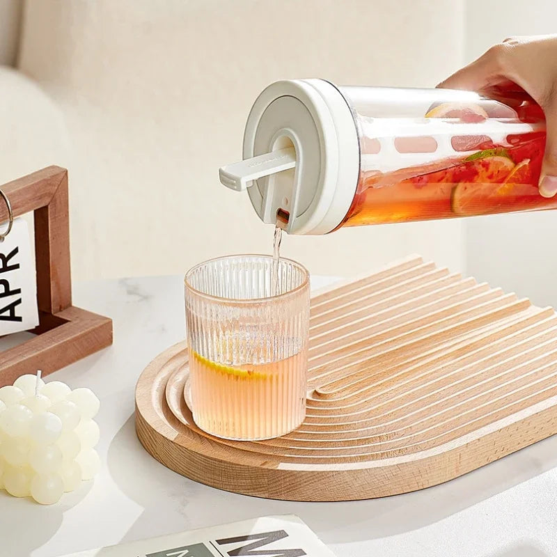 A hand pours iced tea from a glass bottle into a glass, resting on a wooden coaster.