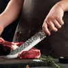 Una mano sostiene un cuchillo de cocina de acero inoxidable forjado cortando carne cruda roja en una tabla de cortar de mader