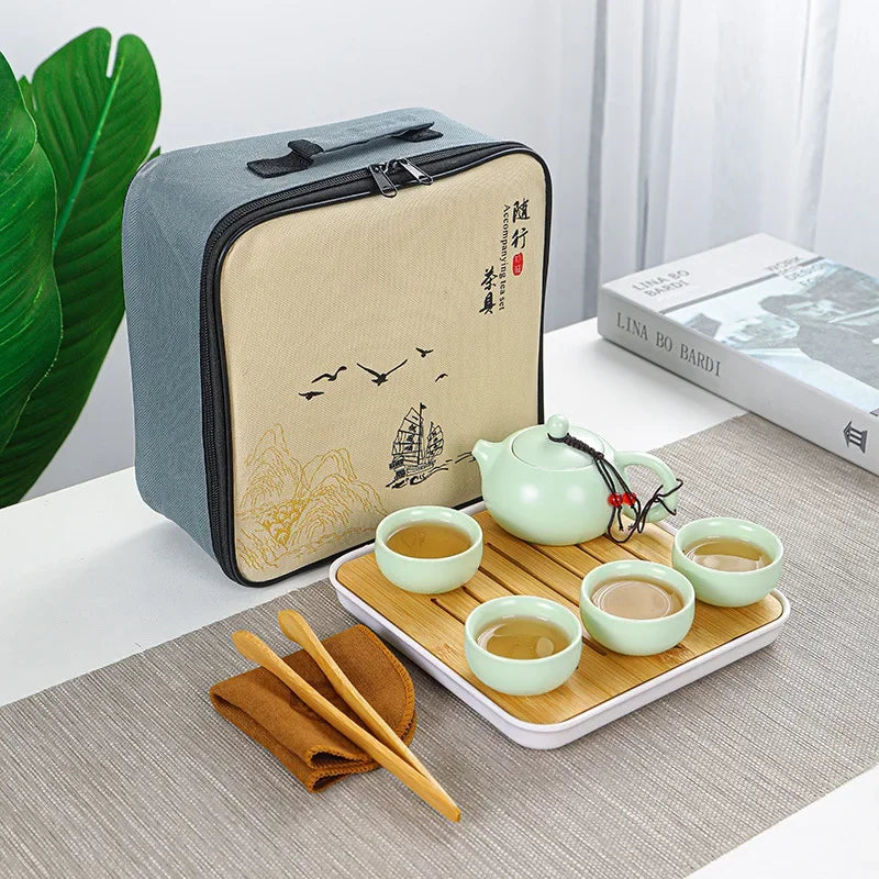 A light gray zippered pouch is shown next to a wooden tray holding a green ceramic tea set with cups and teapot.