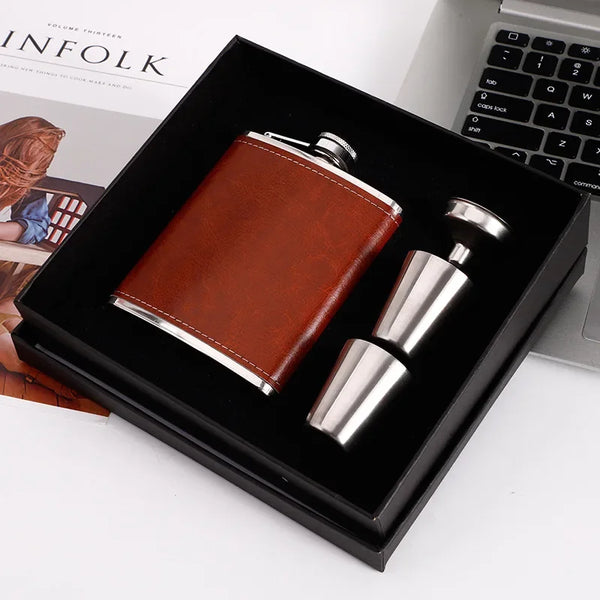 A brown leather hip flask set with stainless steel components displayed in a black box.