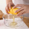 Hands pouring liquid from a yellow egg shell opener into a glass bowl.