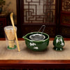 A green ceramic bowl and a metal strainer are displayed on a wooden surface with a bamboo whisk nearby.