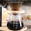 A clear borosilicate glass pour over coffee pot filled with dark brewed coffee, resting on a wooden cutting board.