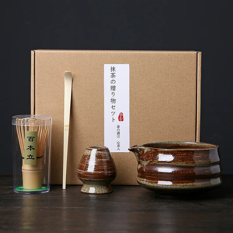 A set of Japanese matcha whisks and a ceramic bowl are displayed in front of a brown box.