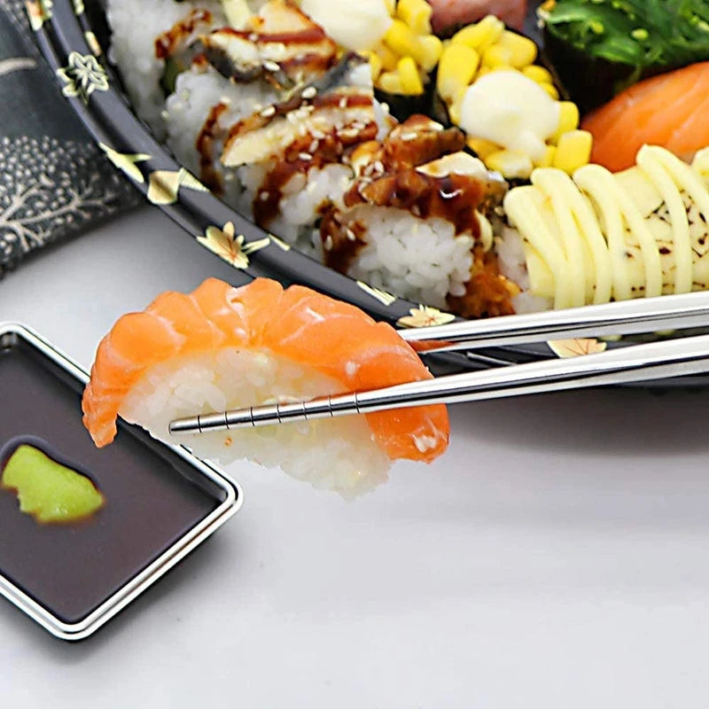 Reusable stainless steel chopsticks holding a piece of orange salmon on rice with various side dishes