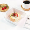 A clear square plastic box holds a slice of bread topped with cream cheese and fresh strawberries and mint leaves.