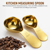 Un jeu de cuillères à mesurer de cuisine en acier inoxydable dorées, tailles 15ml et 30ml, à côté de grains de café.