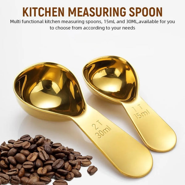 Set goldfarbener Edelstahl-Küchenmesslöffel, 15ml und 30ml, neben Kaffeebohnen.