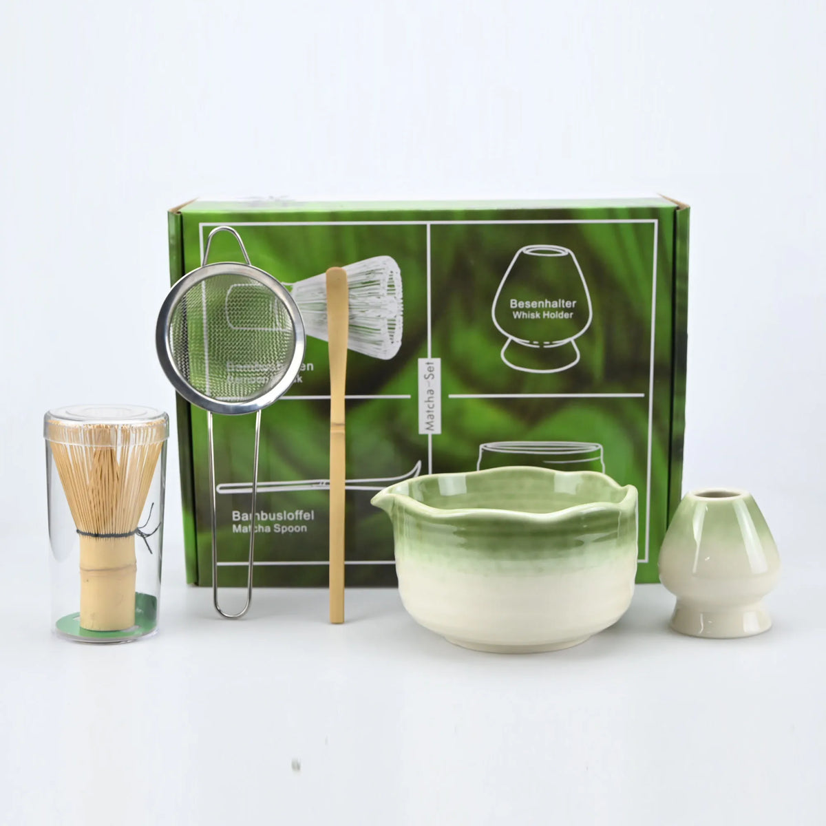 A set of Japanese style matcha bowls and brushes displayed in a green box with various tools.