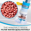 Botella de filtro de agua transparente con tapa amarilla y filtro de malla, junto a un montón de perlas filtrantes rosadas.