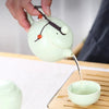 A hand pours liquid from a ceramic teapot into a small bowl, demonstrating an elegant tea ritual.