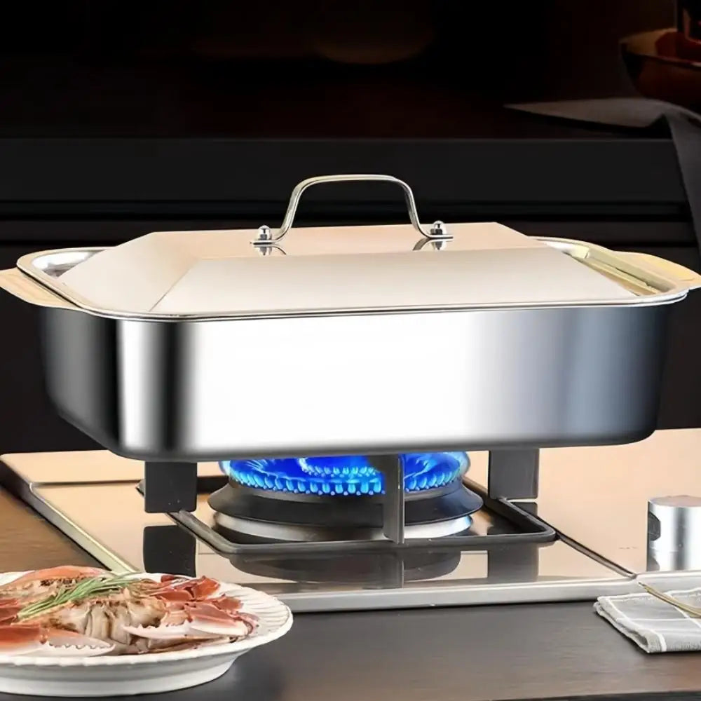 A stainless steel baking pan set with a lid is placed on a portable gas burner for cooking.